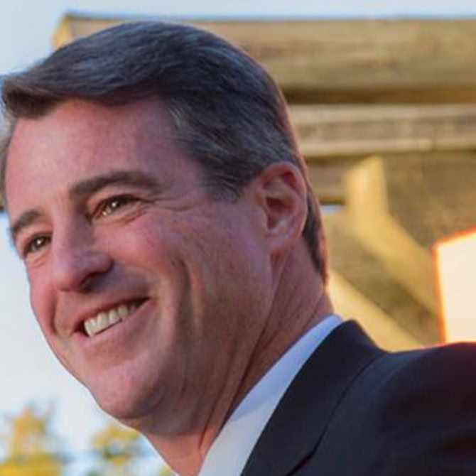 smiling man with short gray hair, wearing dark jacket. he's outside and looking off to the left