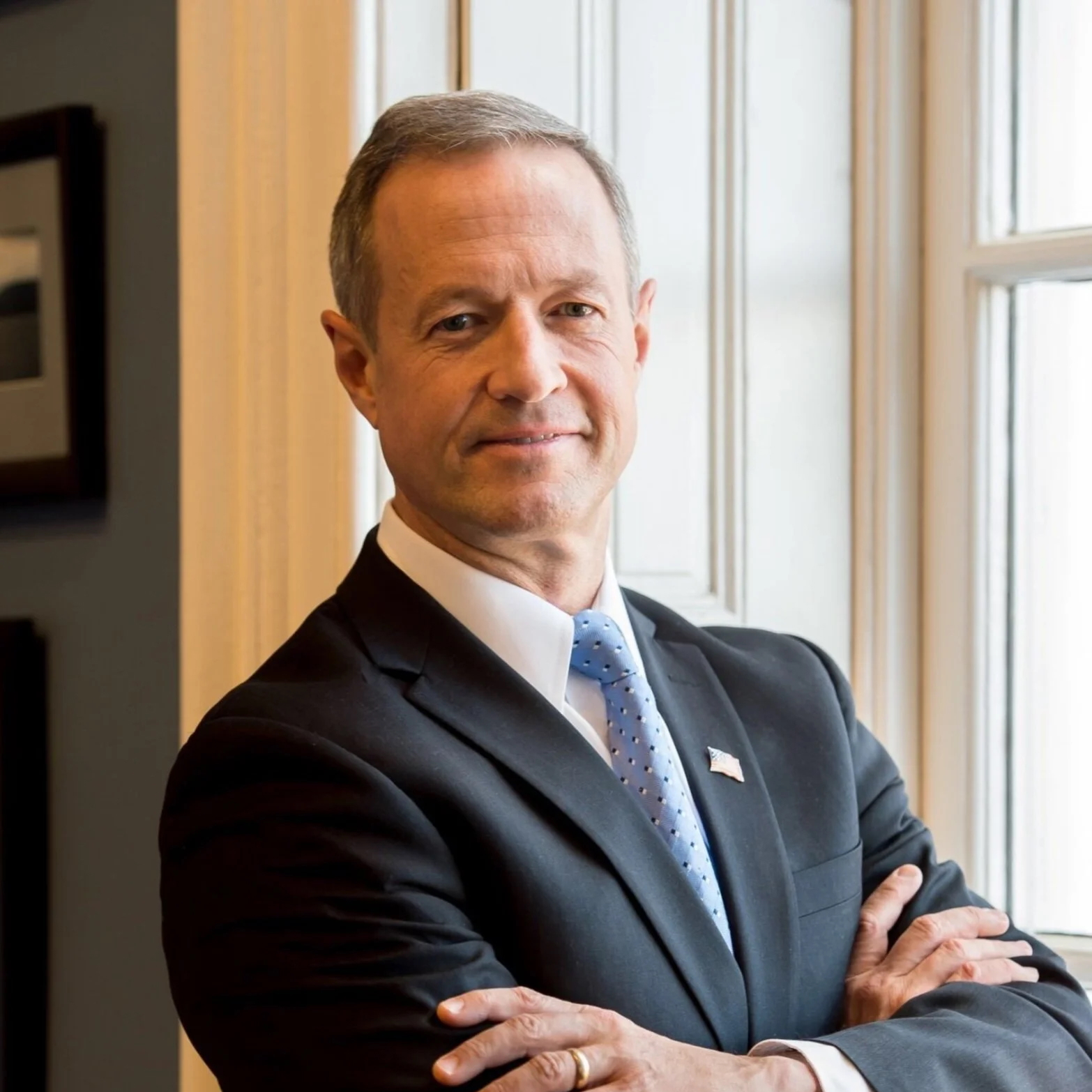 Middle aged man, with arms folded, standing beside a window